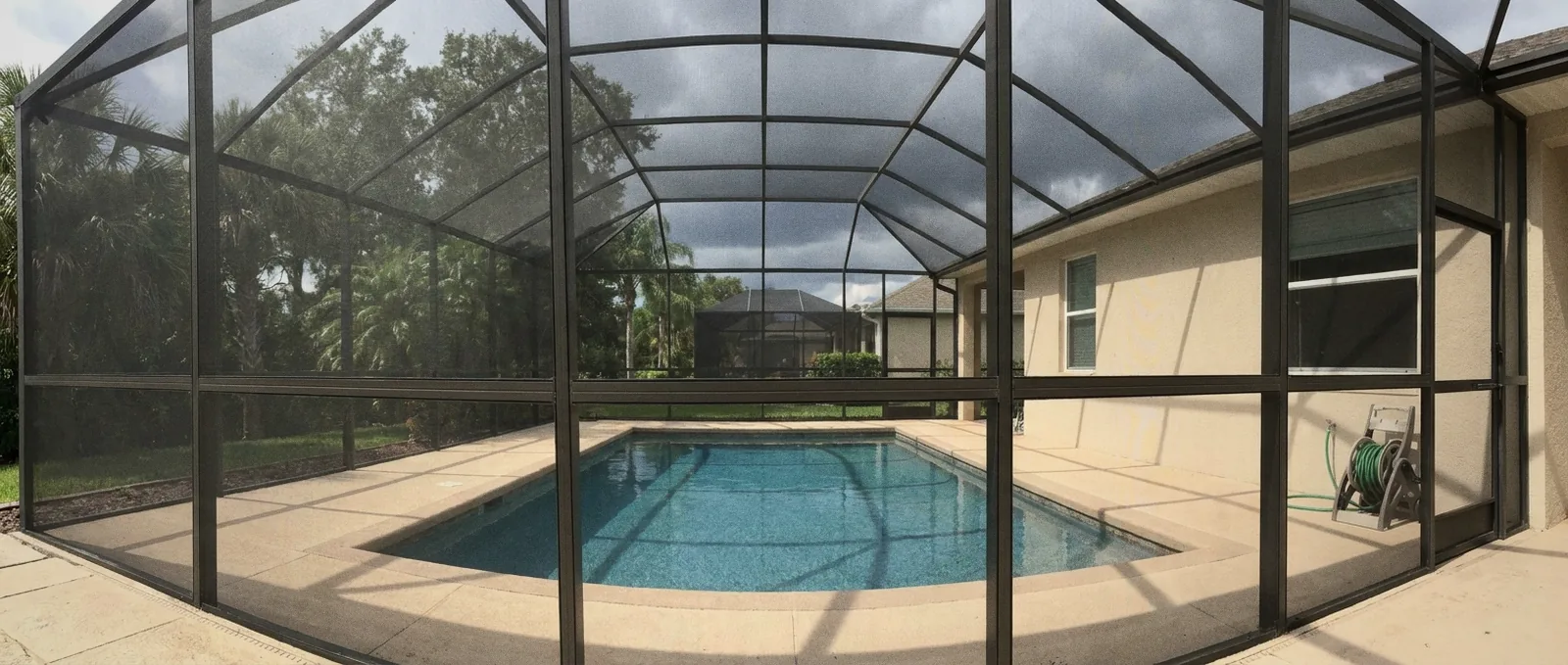 Screened pool behind a Florida home with paver deck under a gray afternoon storm sky